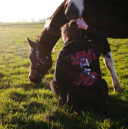 Photo d'un cheval qui broute, avec sa cavalière assise qui porte un hoodie sur le thème du Japon et du cheval. Les motifs sont des érables du Japon, et des kanjis japonais dans lesquels figure un motif de cheval.