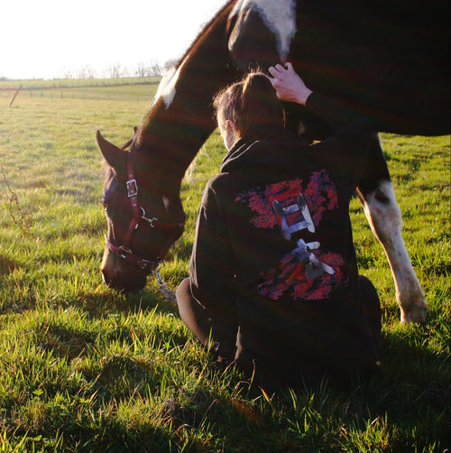 Photo d'un cheval qui broute, avec sa cavalière assise qui porte un hoodie sur le thème du Japon et du cheval. Les motifs sont des érables du Japon, et des kanjis japonais dans lesquels figure un motif de cheval.