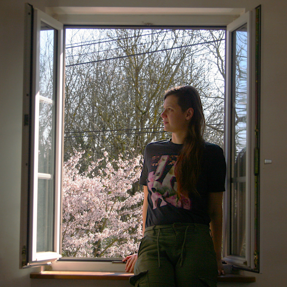 Femme portant un t-shirt sur le thème du Japon, avec un motif de cheval sur des cerisiers du Japon. En arrière-plan, il y a un cerisier en fleurs.