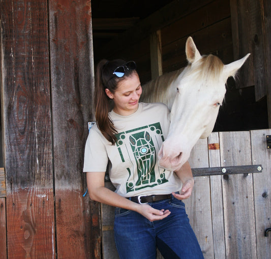 Tshirt beige avec motif de cheval dans les jardins de Versailles, porté par une cavalière avec son cheval à côté d'elle